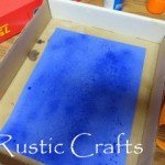 Demonstration for spraying adhesive on paper inside a box.